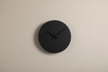 Contemporary black wall clock with clean lines on a plain neutral background, realistic photo